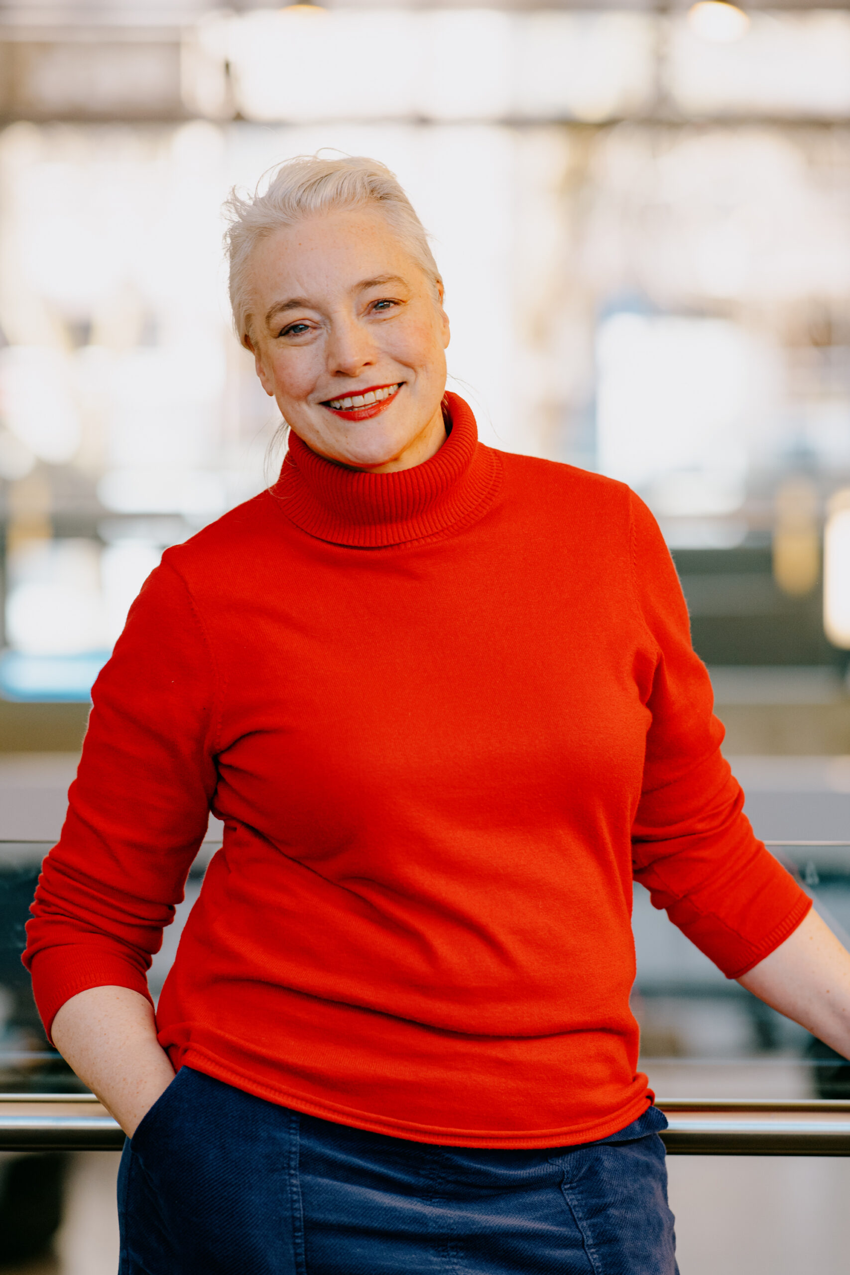 Elspeth Murray, a white woman with tied-back silver hair wearing a red polo-neck jumper and denim skirt.